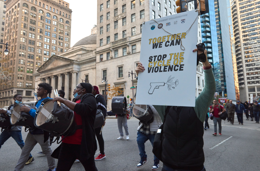 A woman, standing in a city street, holds a sign that says Together We Can Stop the Cycle of Violence